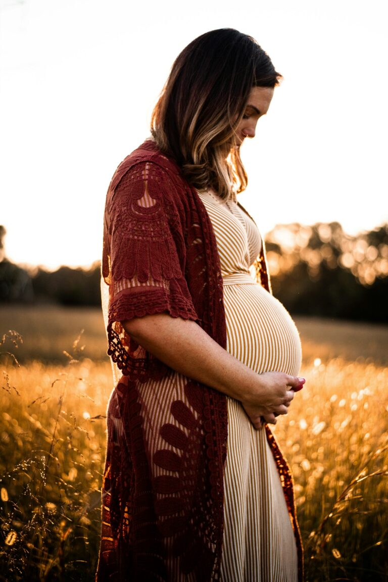 Une femme enceinte regarde son ventre arrondi au milieu d’un champ de blé.